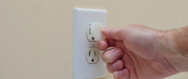 Image of a hand installing a child safety plug into an electric wall outlet.