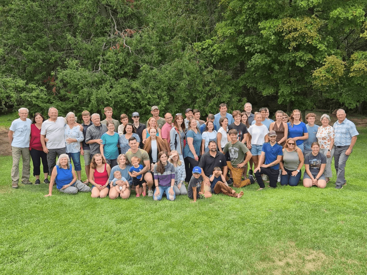 Large diverse group of adults and children posing on a grassy lawn with trees in the background.