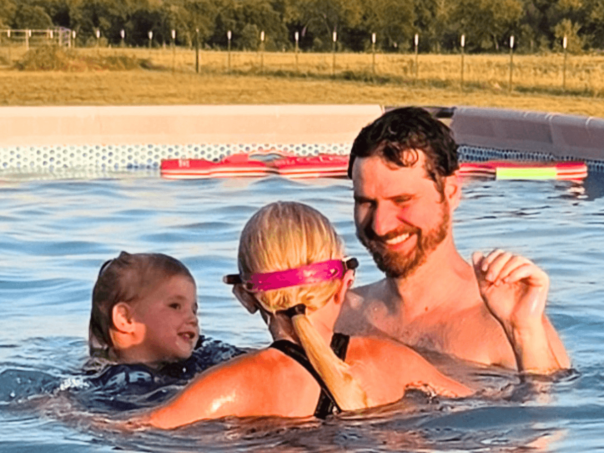Man with a beard and two children smiling while swimming in a pool on a sunny day.