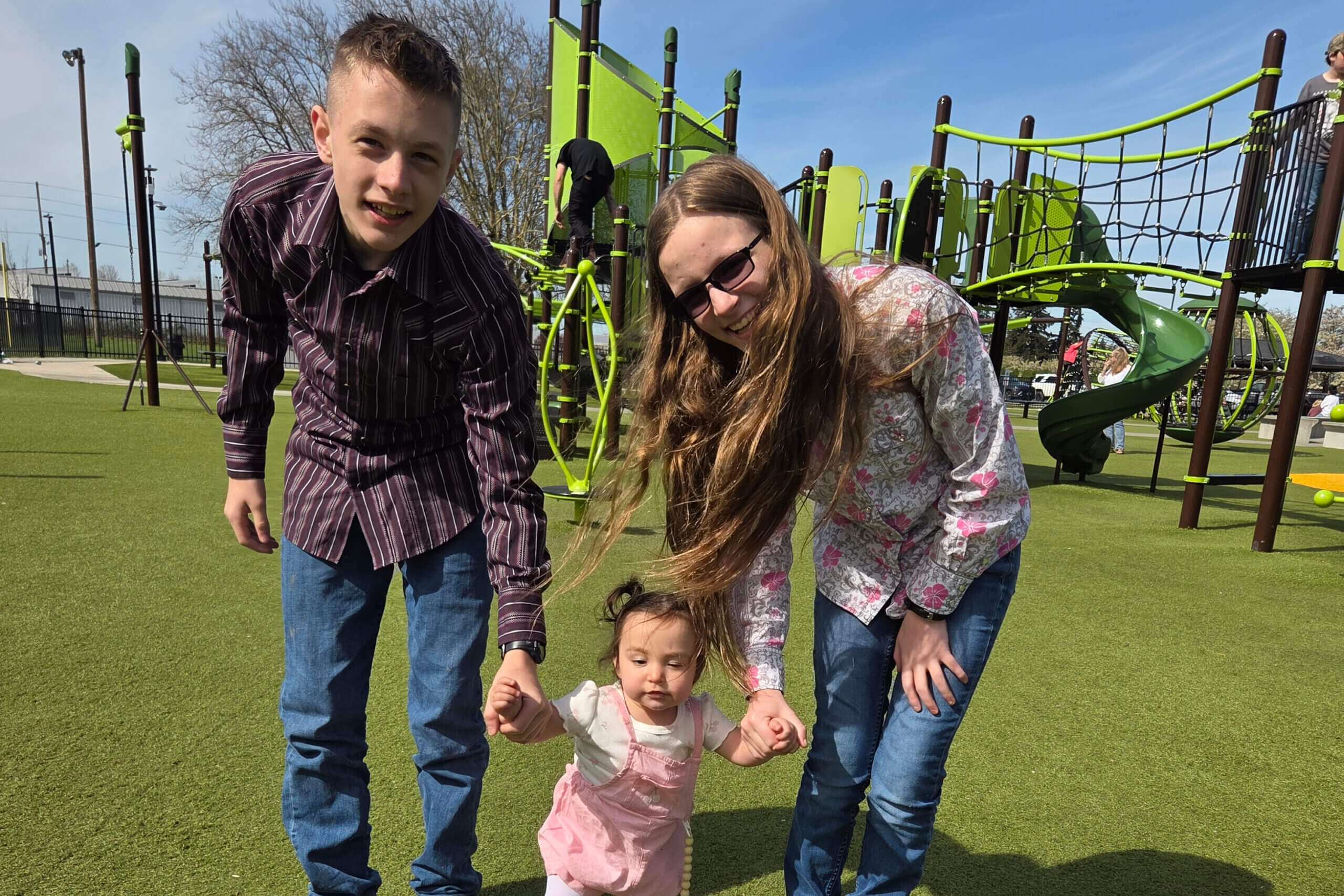 Family of four playing together on a bright playground with green turf and colorful equipment in the background.