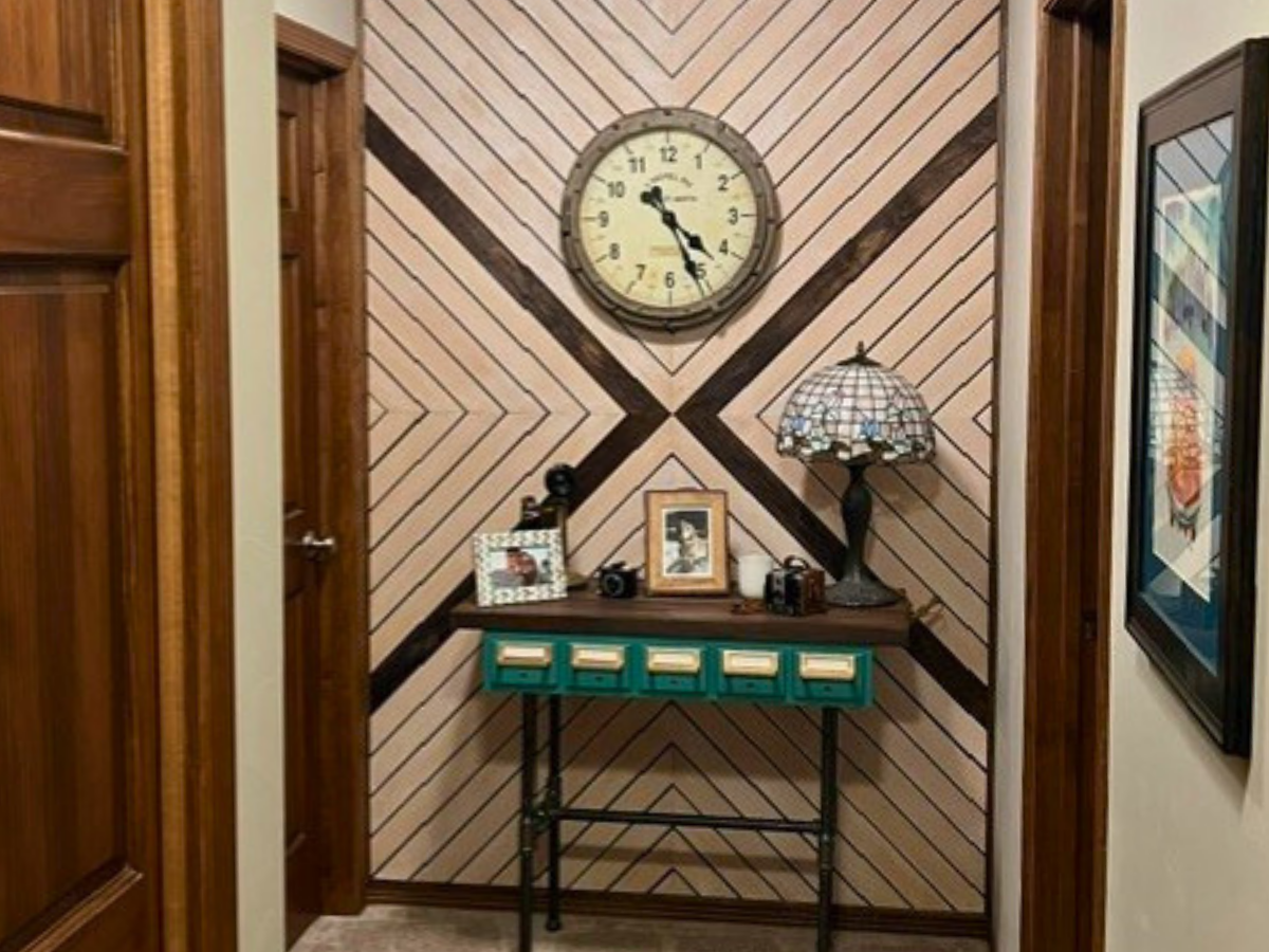 Wall hallway corner featuring a round clock above a wooden console table with teal drawers and a Tiffany-style lamp.