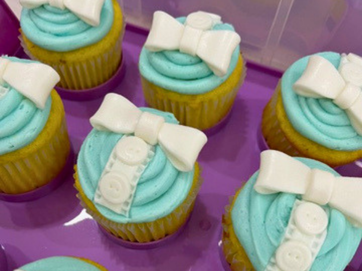 Cupcakes with turquoise frosting topped by white fondant bows on a purple tray.