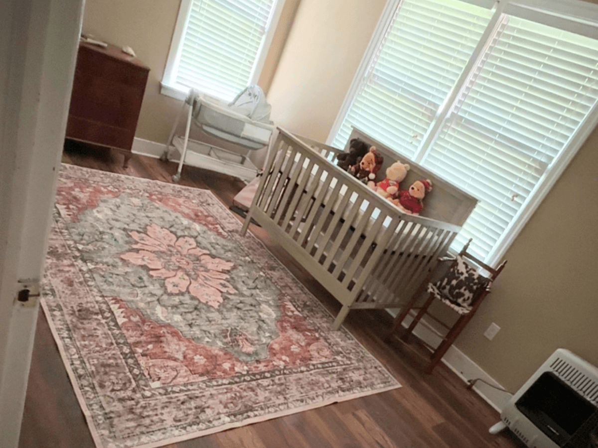 Nursery with a gray crib, stuffed animals on top, dresser, rocking chair, and a large floral rug.