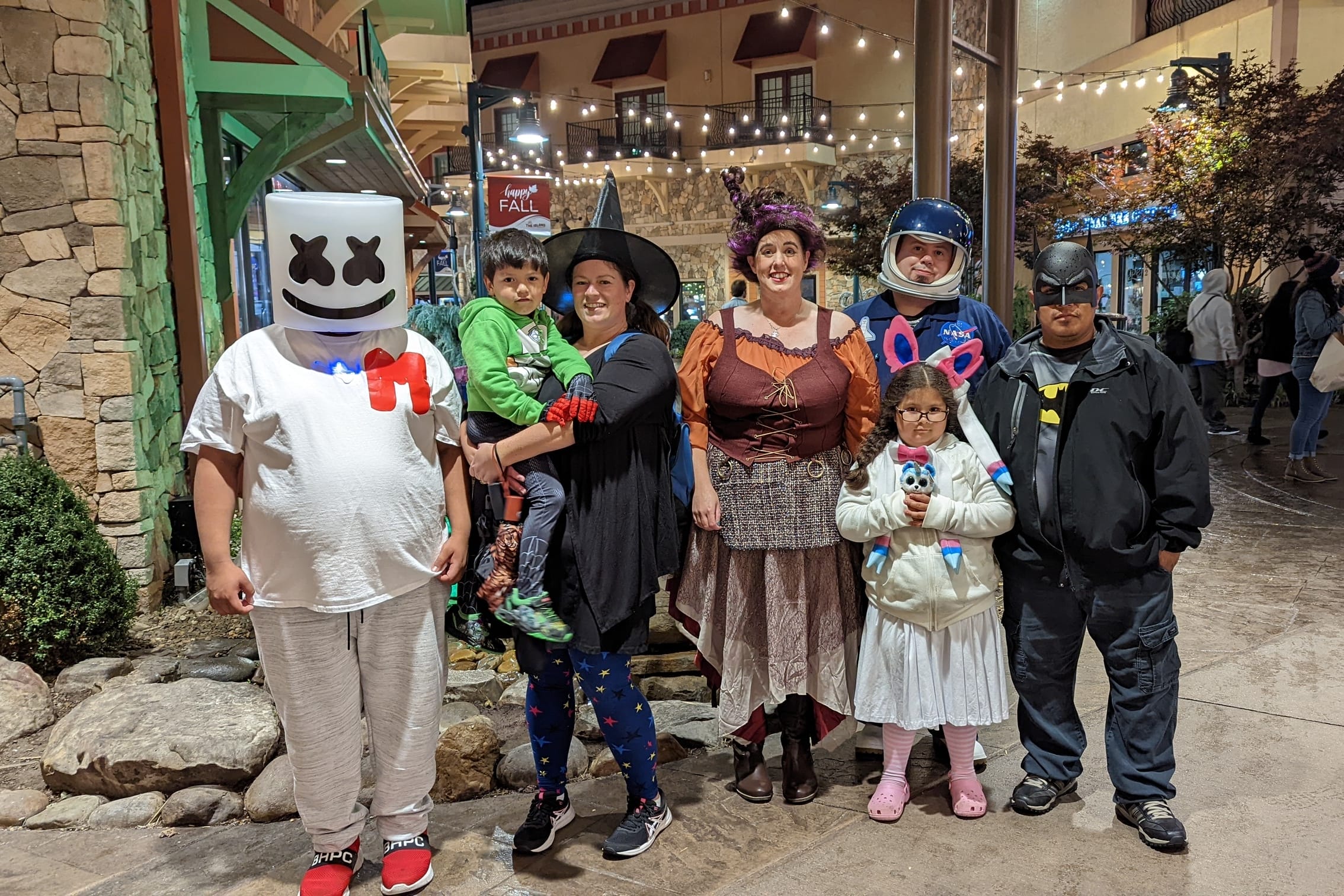 Group of people in Halloween costumes posing together at night in a decorated outdoor area.
