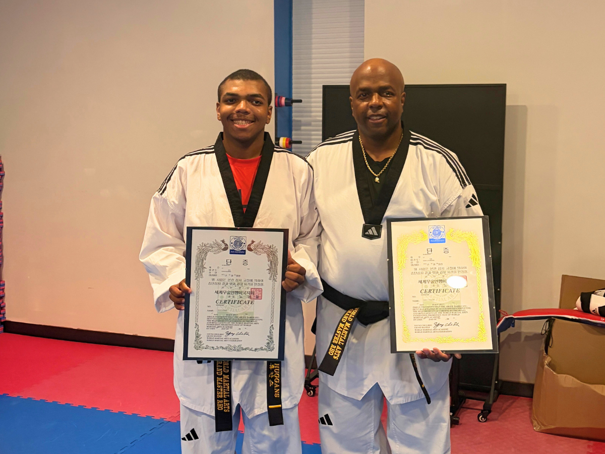 Two men in white Taekwondo uniforms pose with framed certificates, smiling at the camera.
