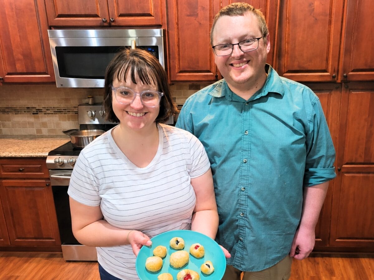 Smiling couple in a kitchen proudly displaying a turquoise plate of small baked pastries.