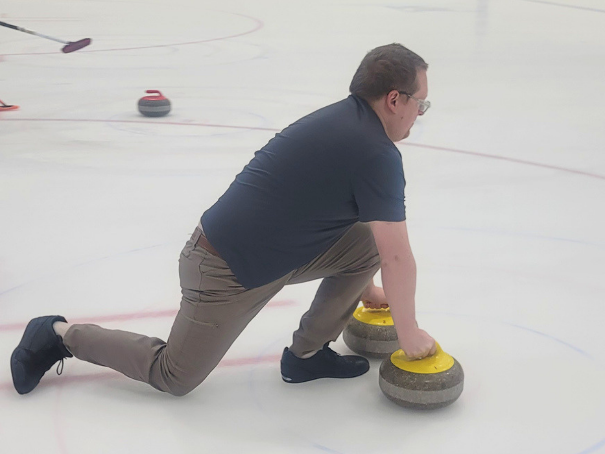 Man curling on ice in a deep lunge, releasing a yellow-handled stone.