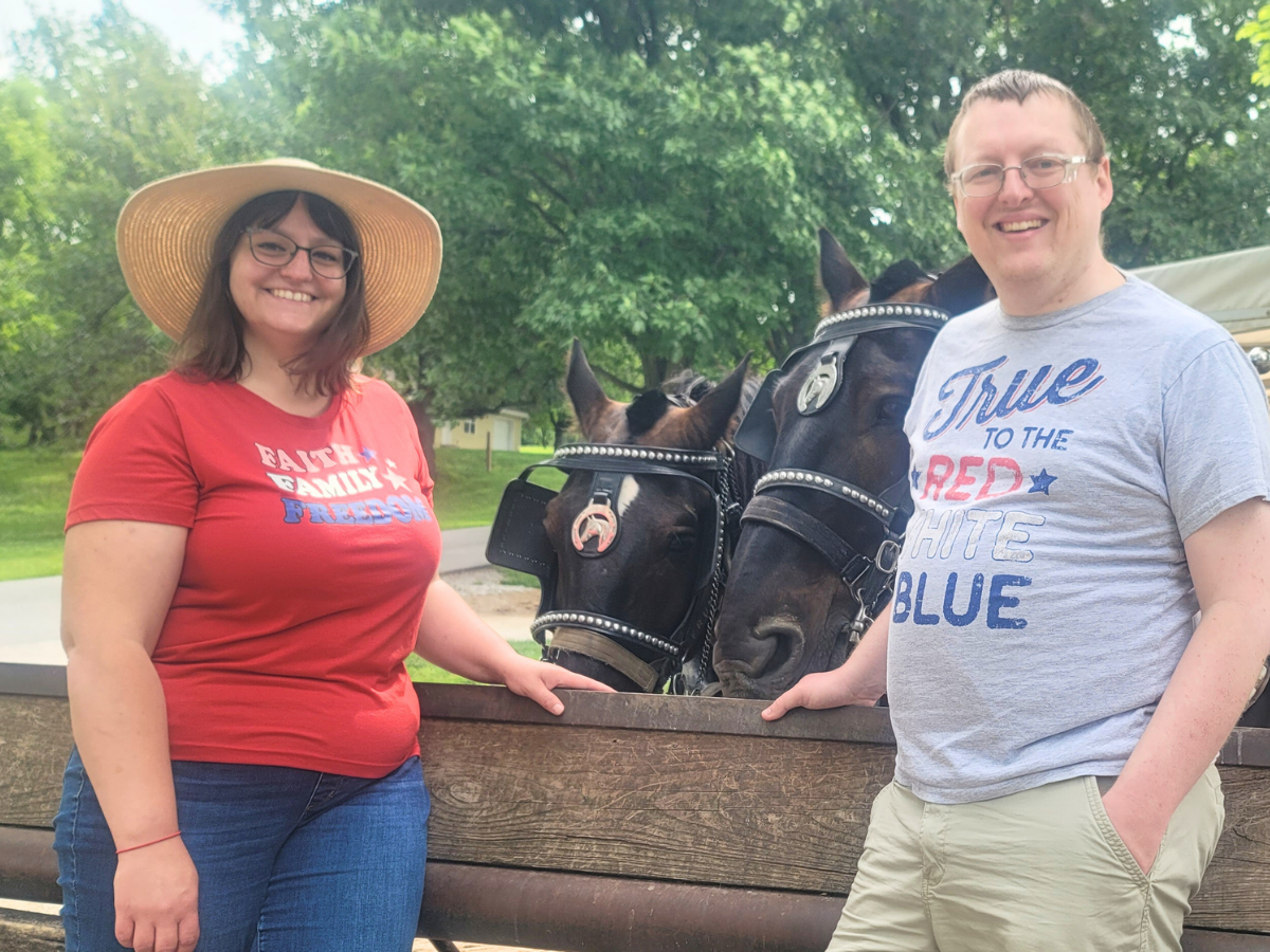 Couple posing with two bridled horses behind them in an outdoor park setting.