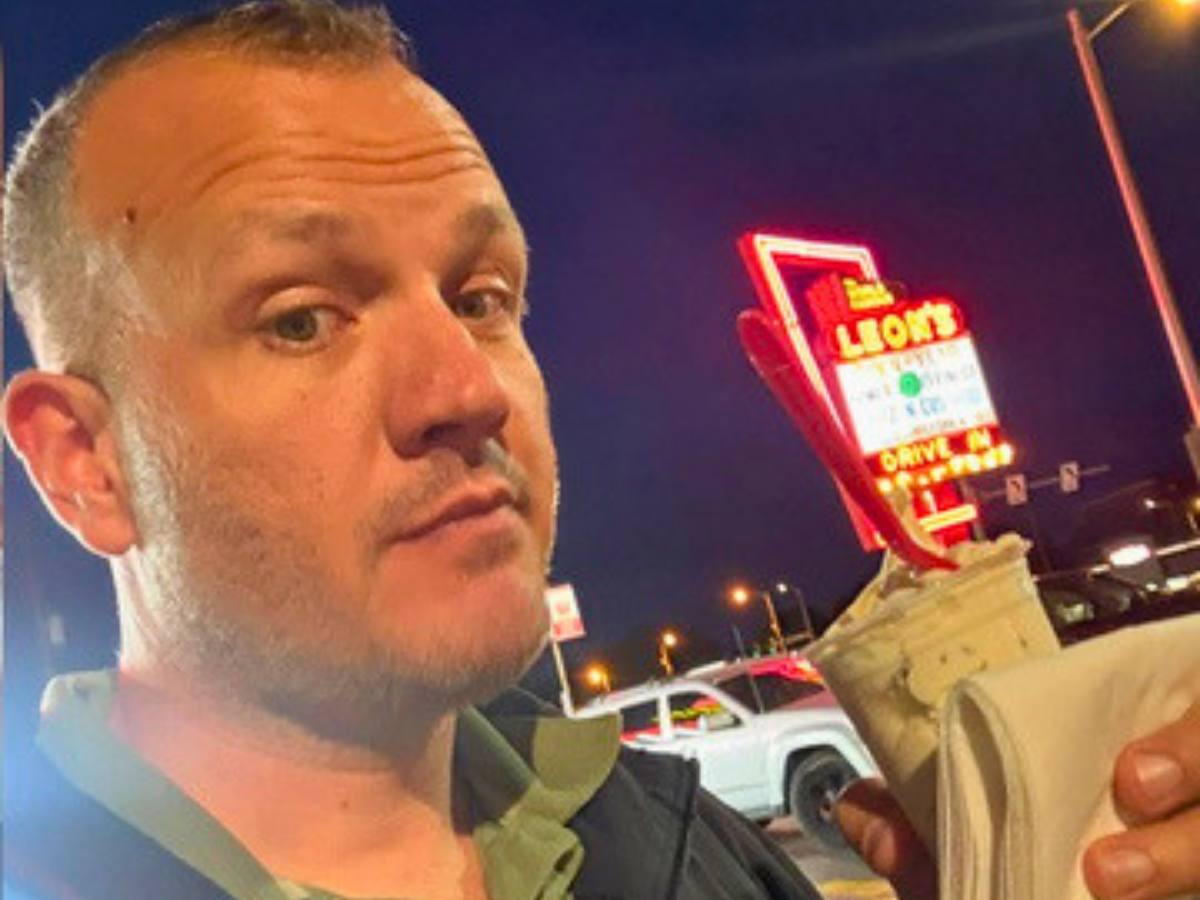 Close-up of a man taking a selfie at night in a parking lot, with a bright red neon sign in the background.