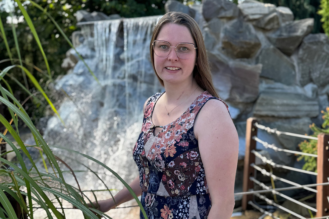 Portrait of a woman with glasses standing outdoors by a rocky waterfall.