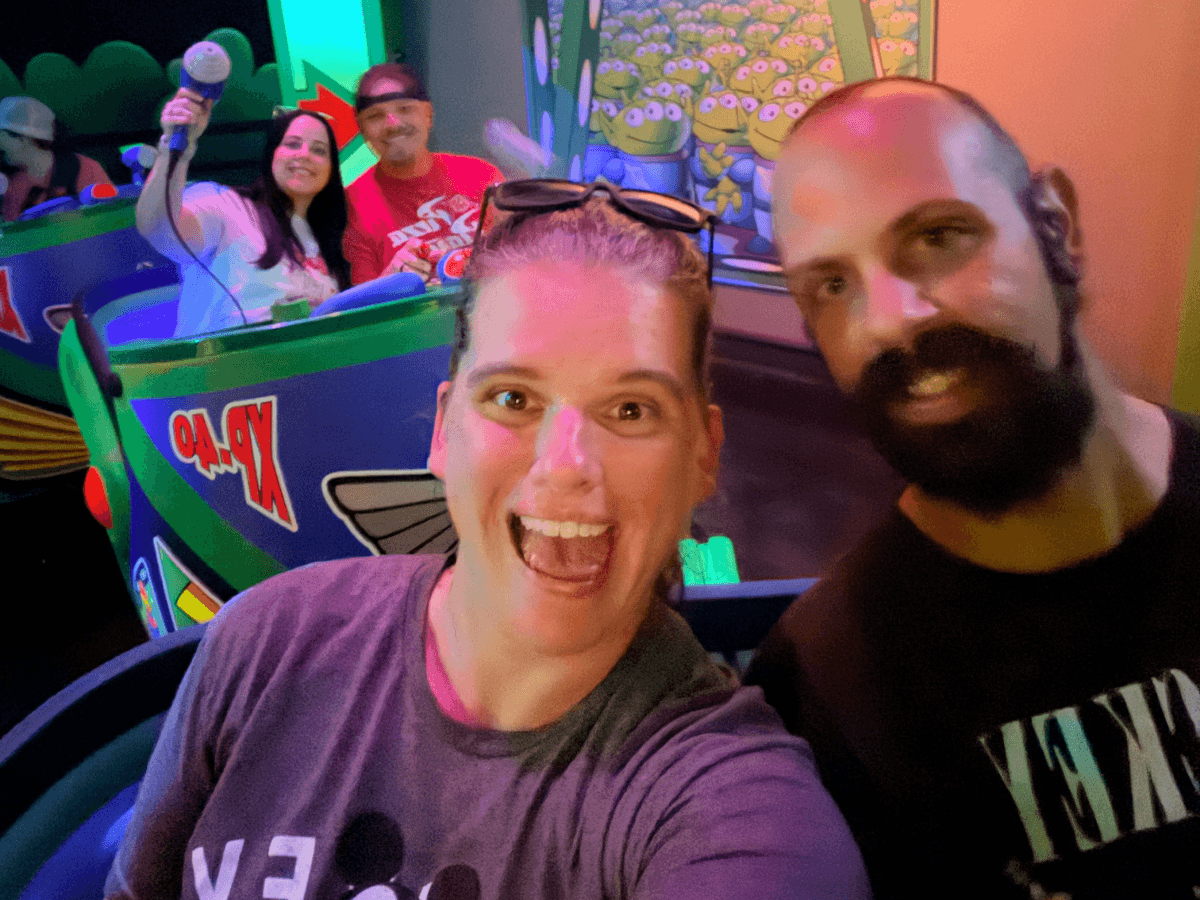 Smiling woman and man on a colorful amusement ride, taking a selfie with anticipation and excitement visible in their faces.