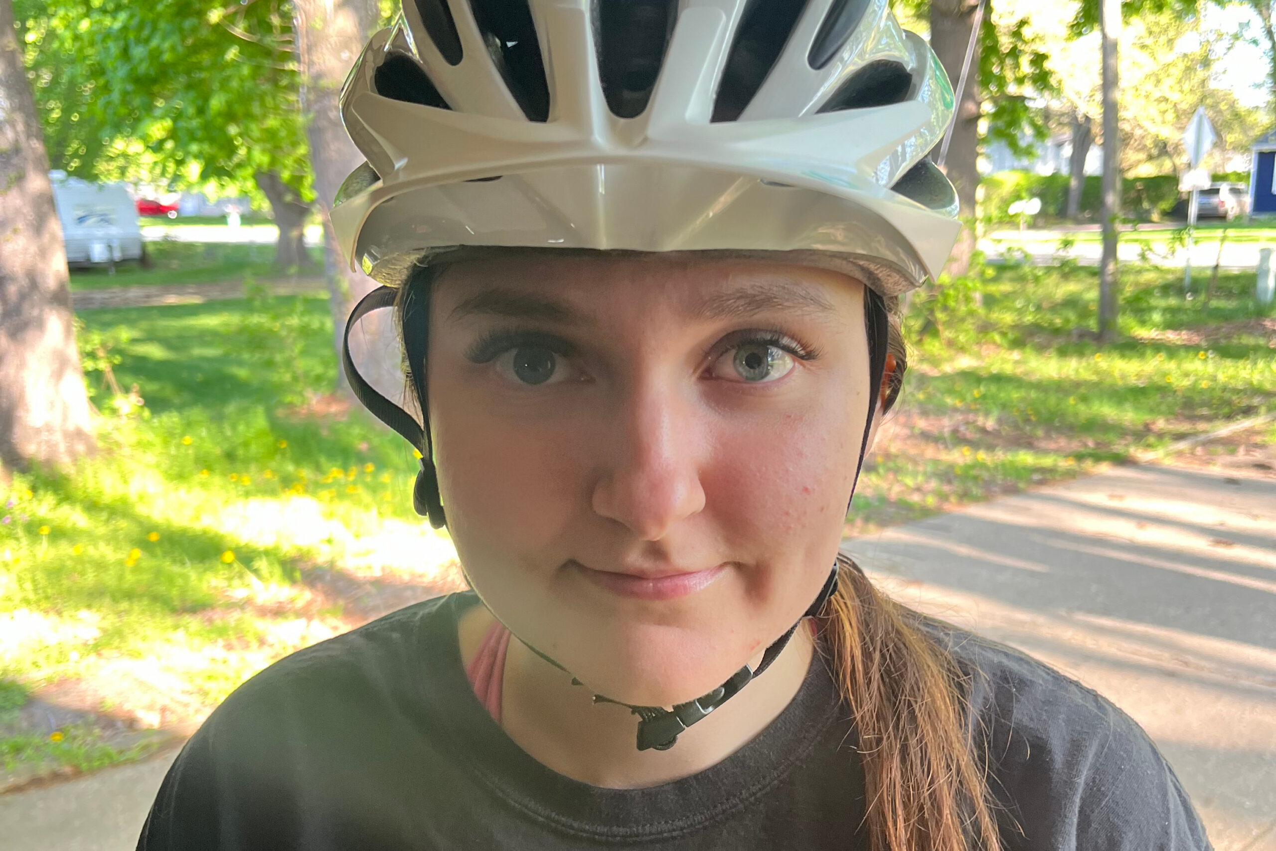 Close-up of a person wearing a white bike helmet outdoors in a sunny leafy park.