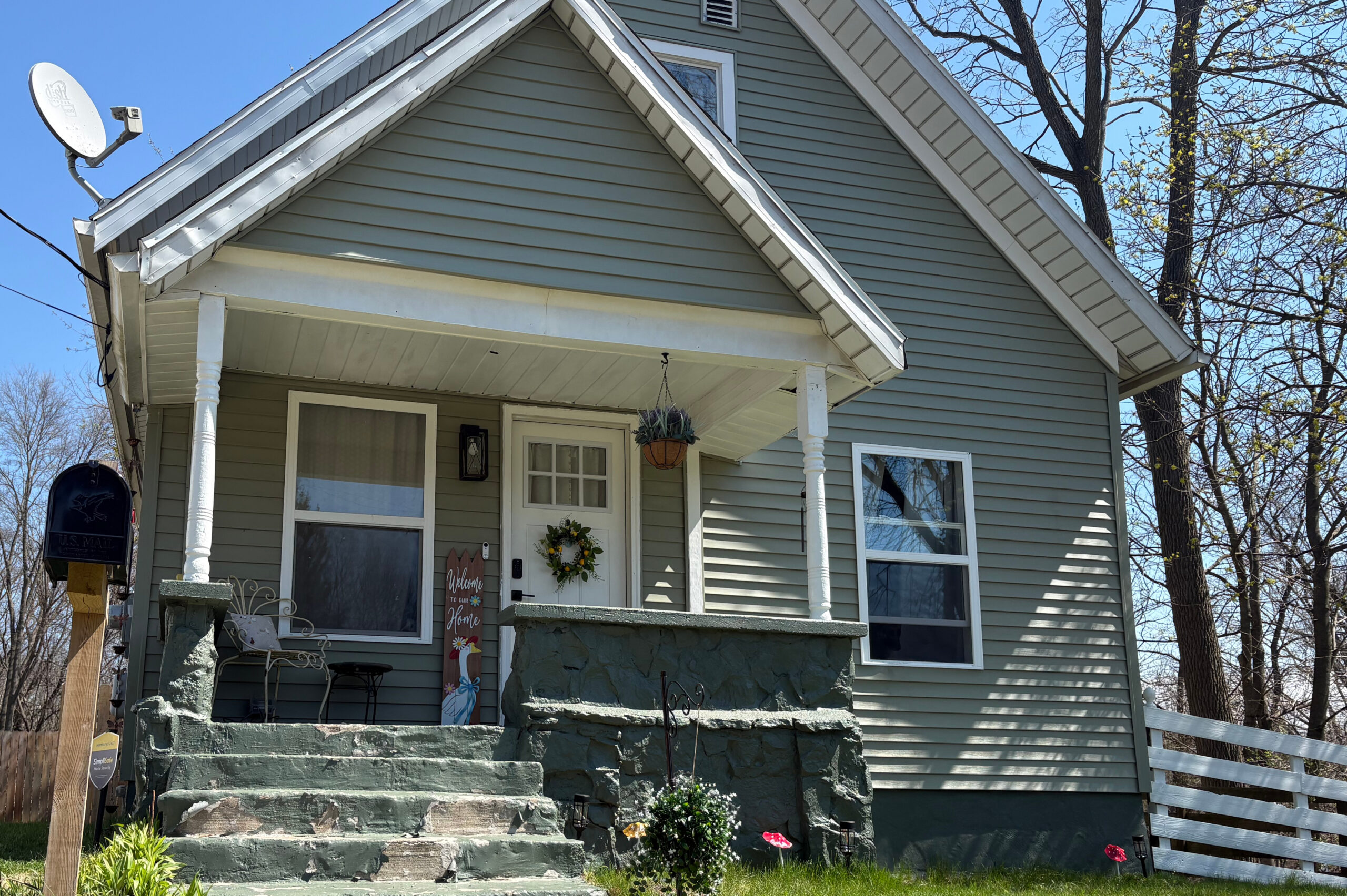 Front view of a light-green house with a covered porch, white trim, and a stone staircase leading to the door.