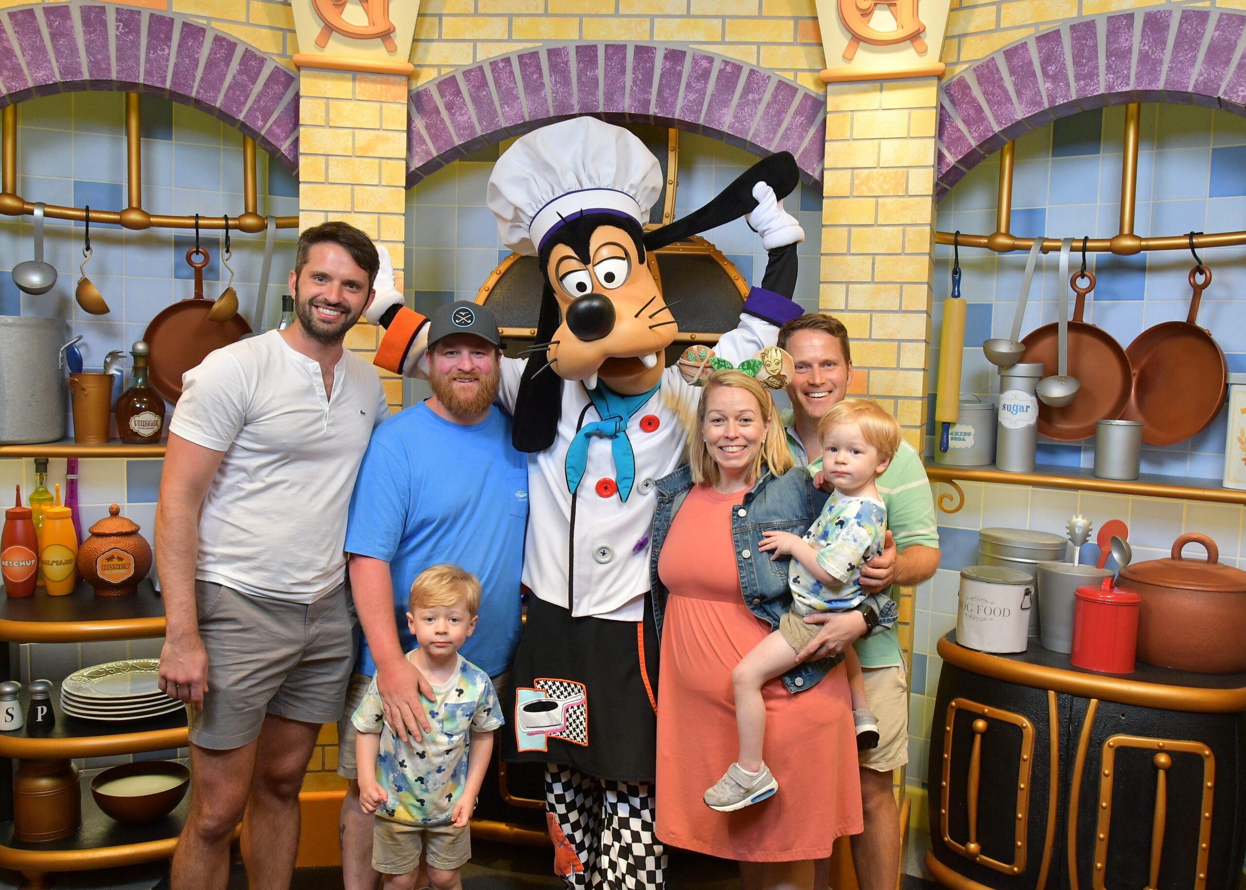 Family posing with Goofy in a chef outfit in a colorful kitchen set.