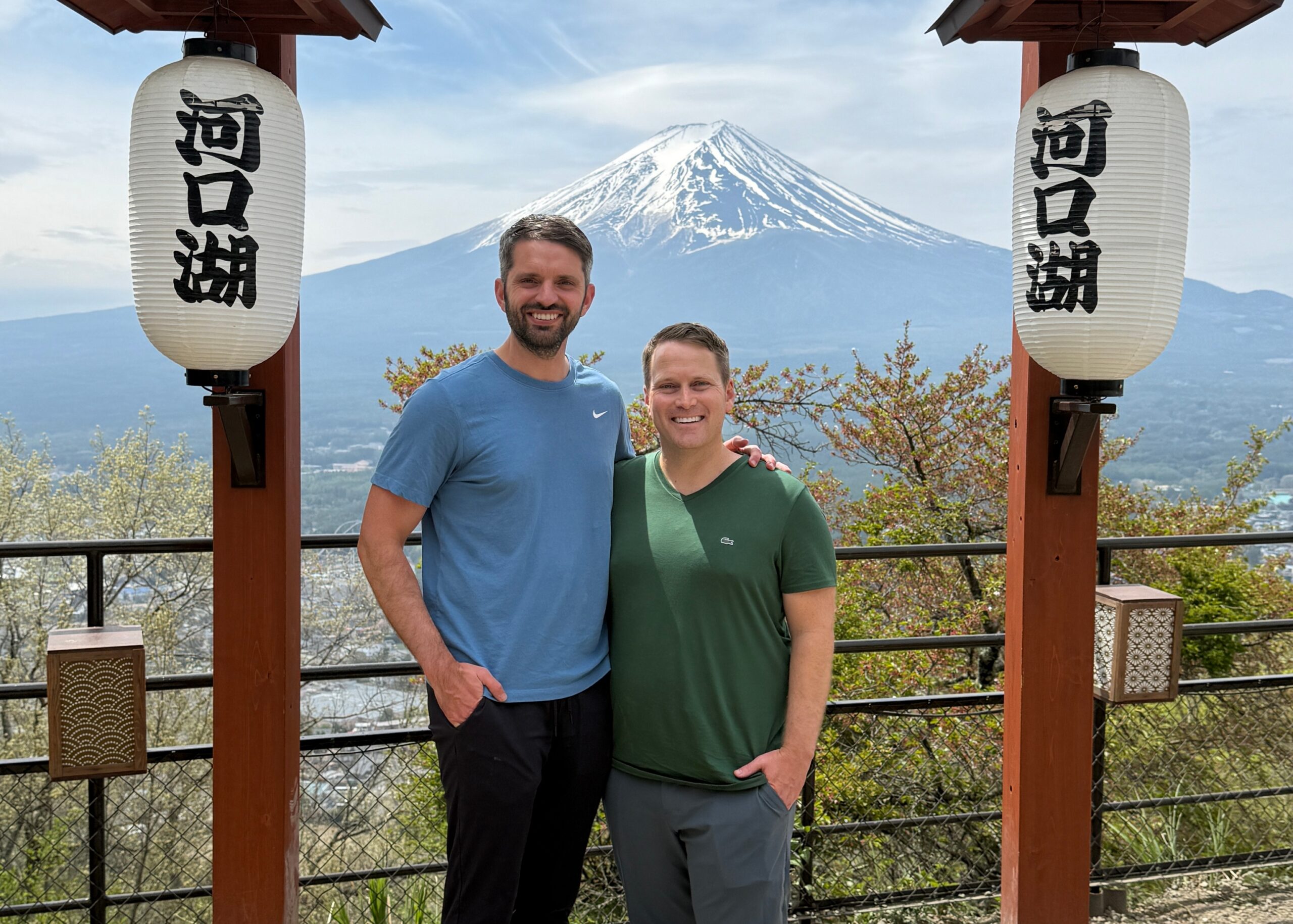 Two men posing together on a railing with Mt. Fuji in the background and large white lanterns on either side.
