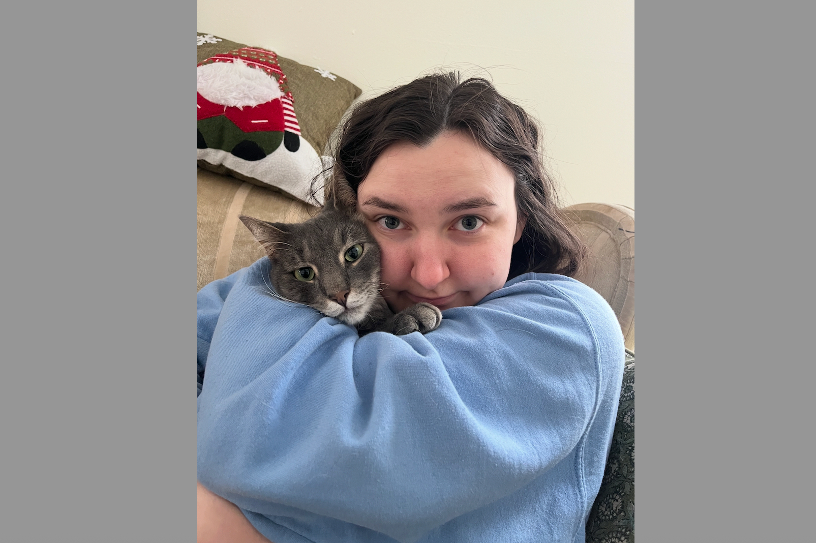 Woman cuddling a gray cat in a blue sweatshirt on a couch.