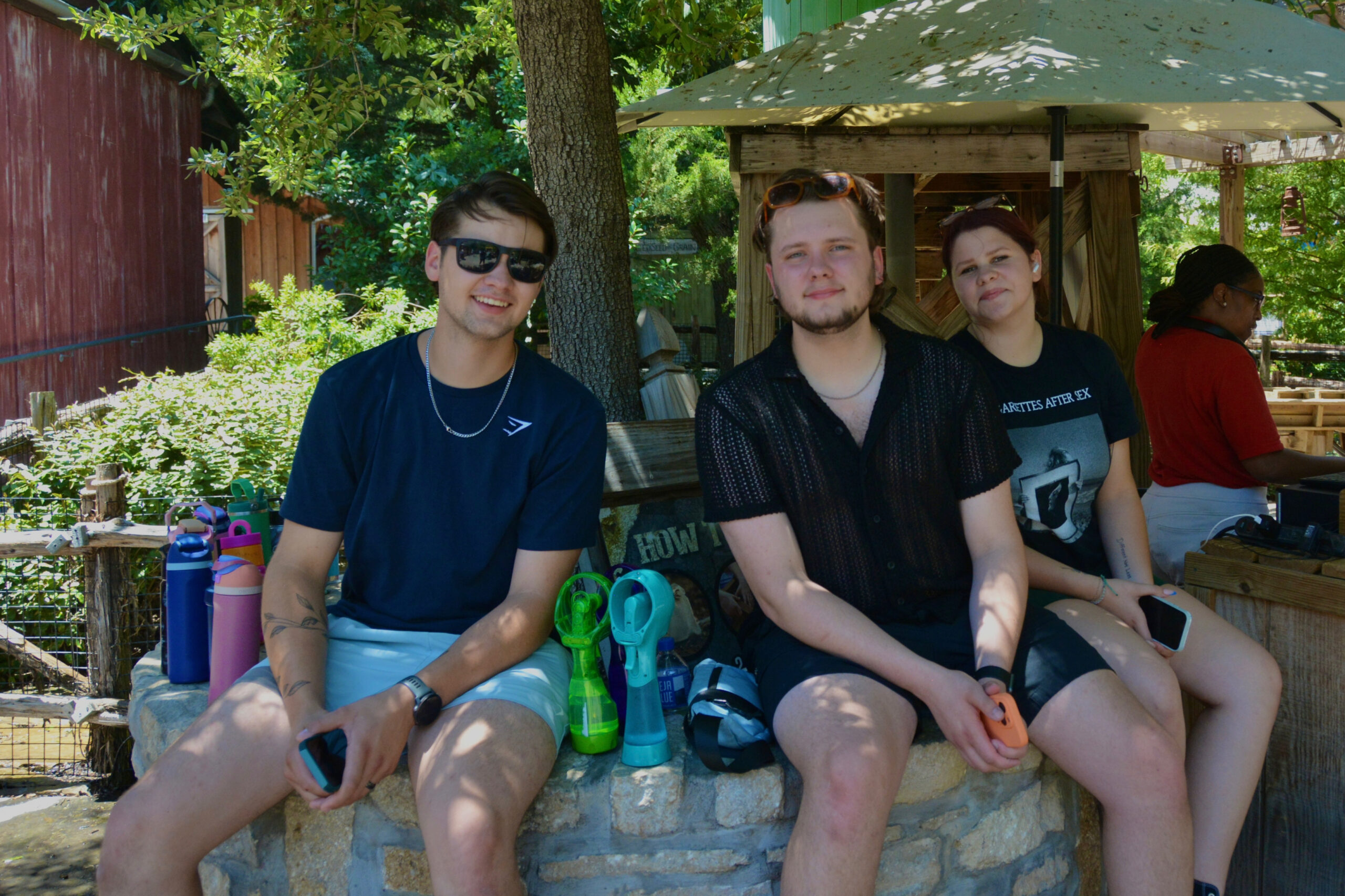 Four friends sitting on a stone bench outdoors, smiling, with water toys and greenery around.