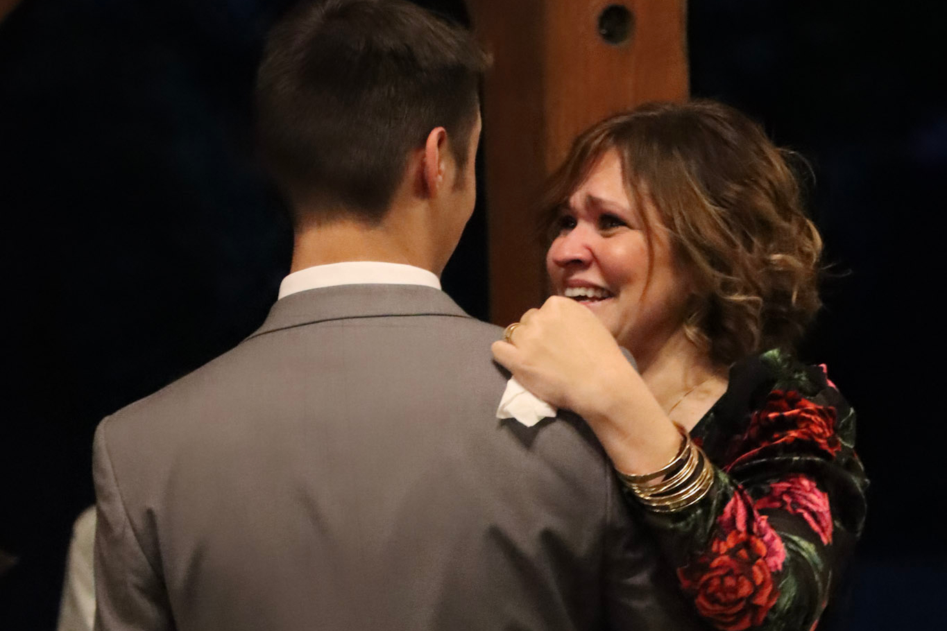 Woman embracing a man in a gray suit, smiling through tears at a nighttime event.