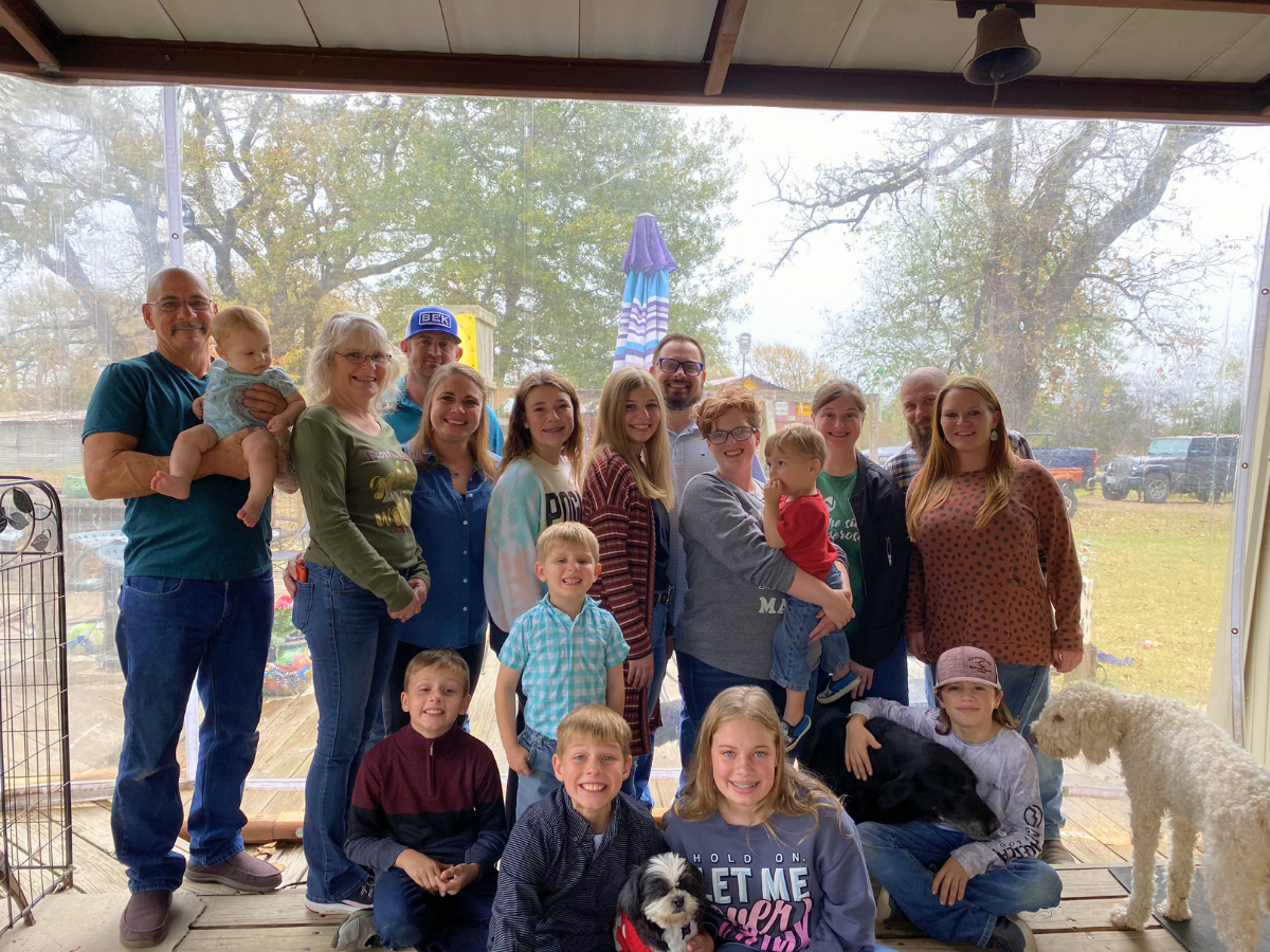 Large group of people of various ages posing for a photo on a porch, with dogs nearby.