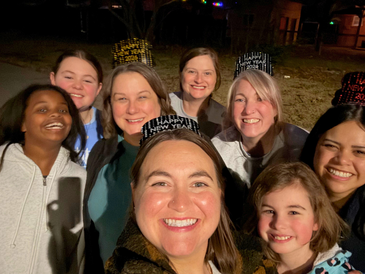 Smiling group of friends and family taking a nighttime selfie, wearing Happy New Year party hats outdoor.