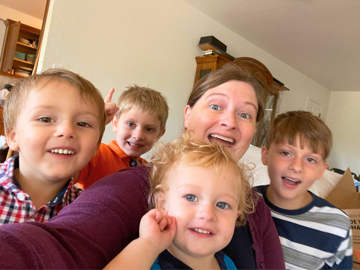 Group selfie of a woman with four young children smiling at the camera in a living room.