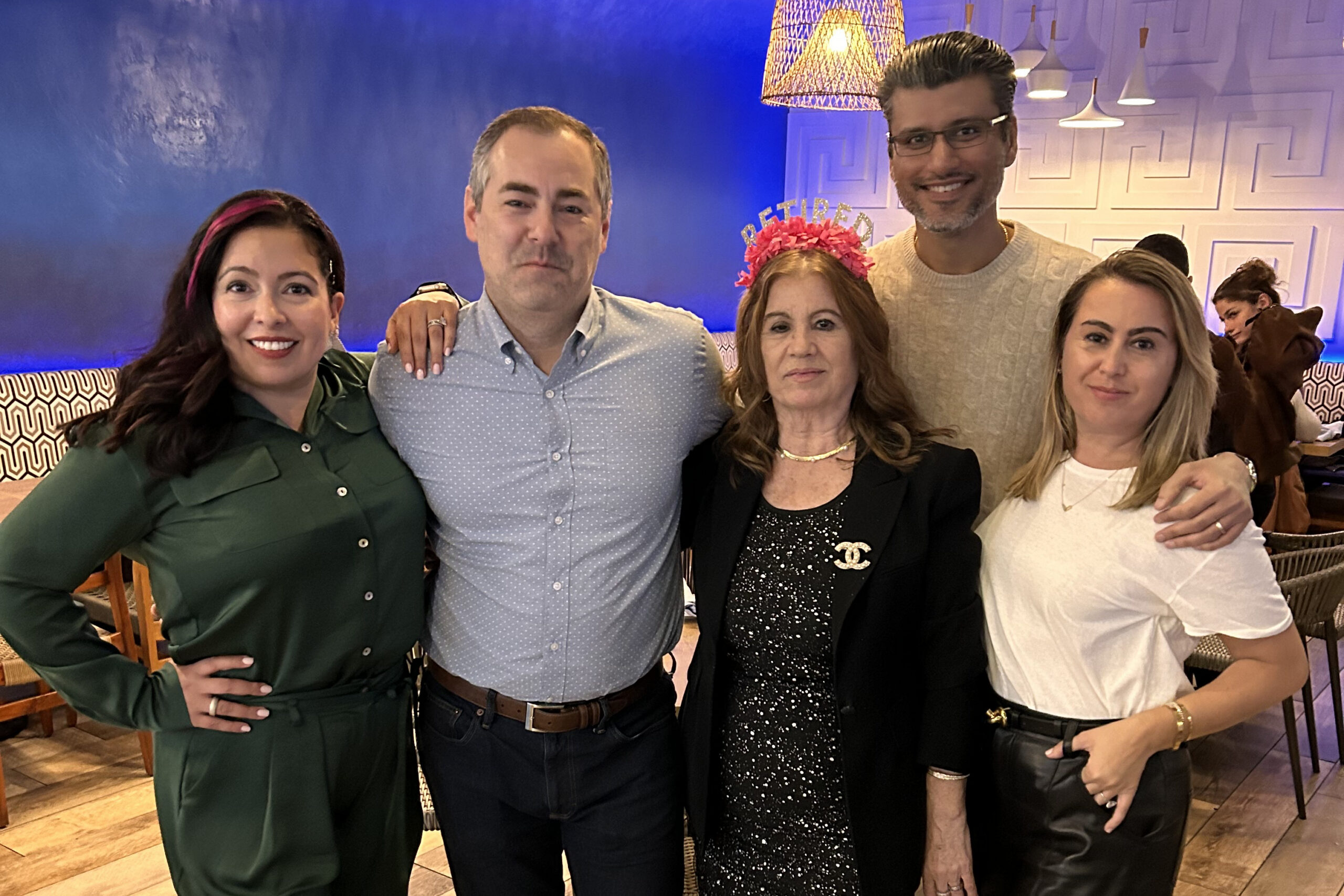 Five adults posing together in a restaurant, smiling at the camera.