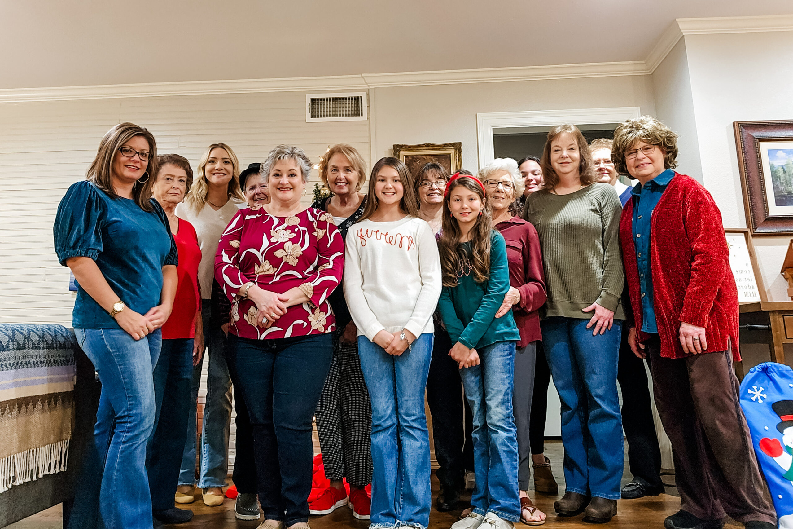 A large group of women and two young girls posing together in a living room for a group photo.