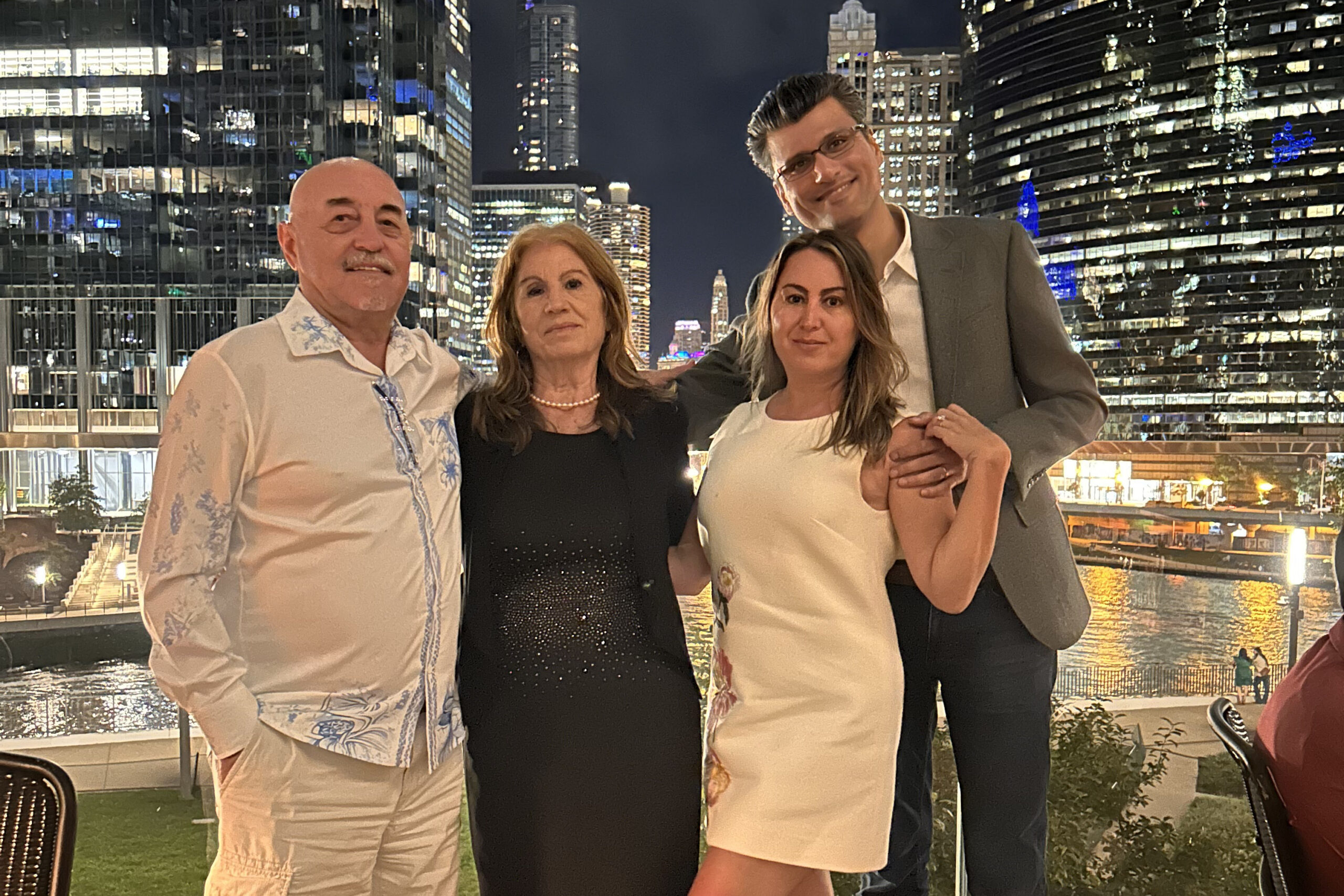 Four adults posing on a rooftop at night with illuminated skyscrapers in the background.