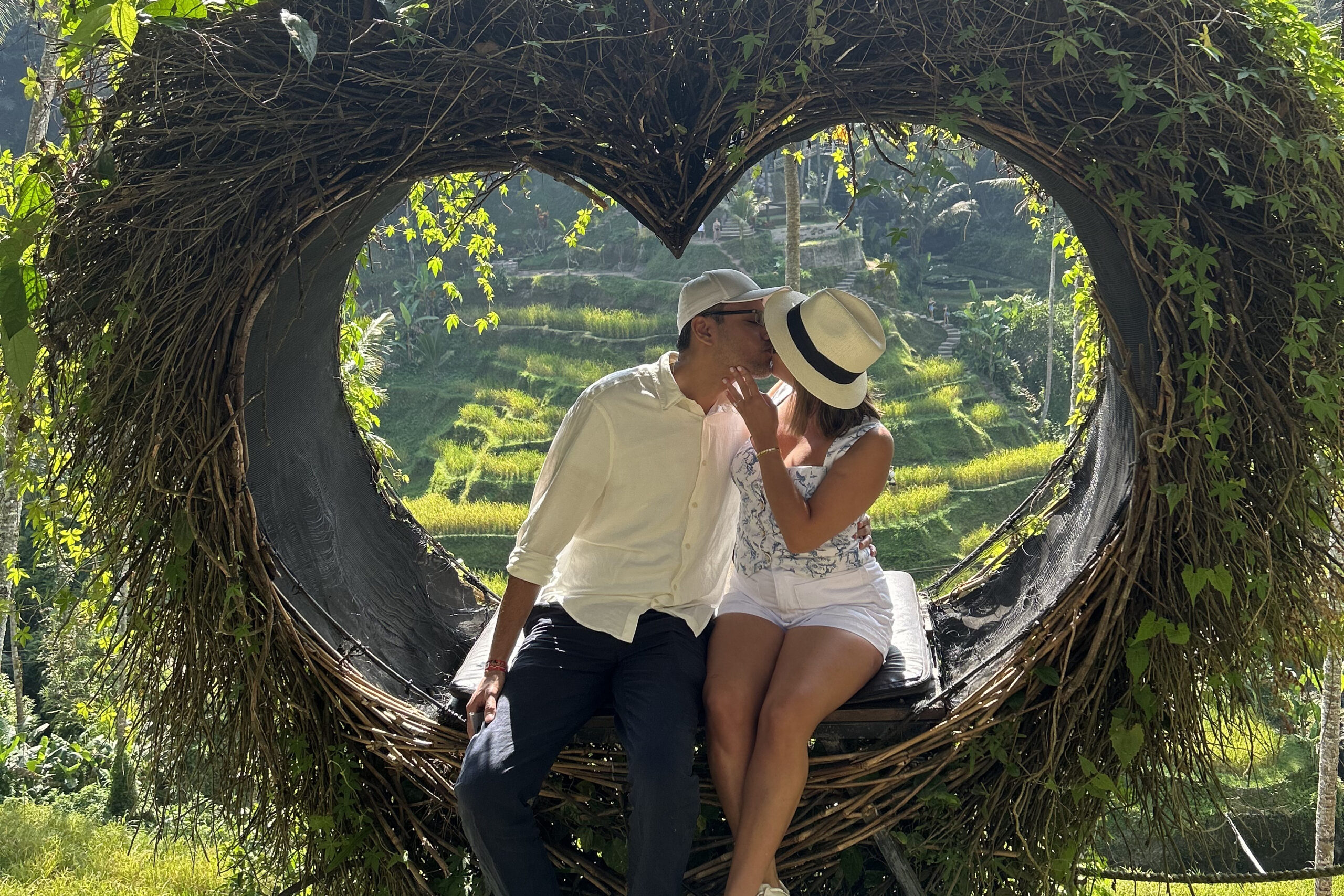 Couple sharing a kiss inside a large woven vine tunnel with greenery and terraced fields in the background