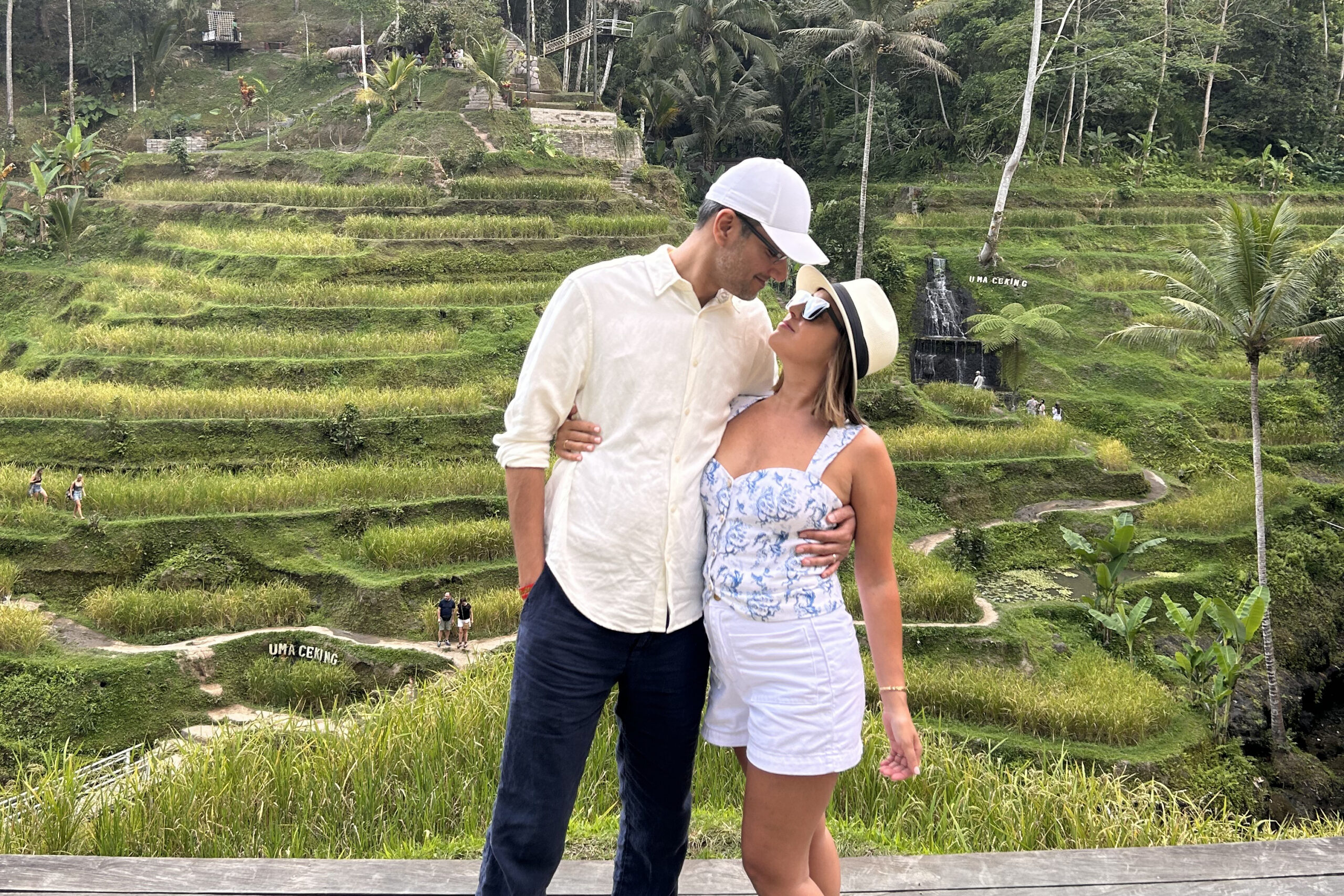 Couple standing and embracing on a wooden ledge with green terraced rice fields behind them.