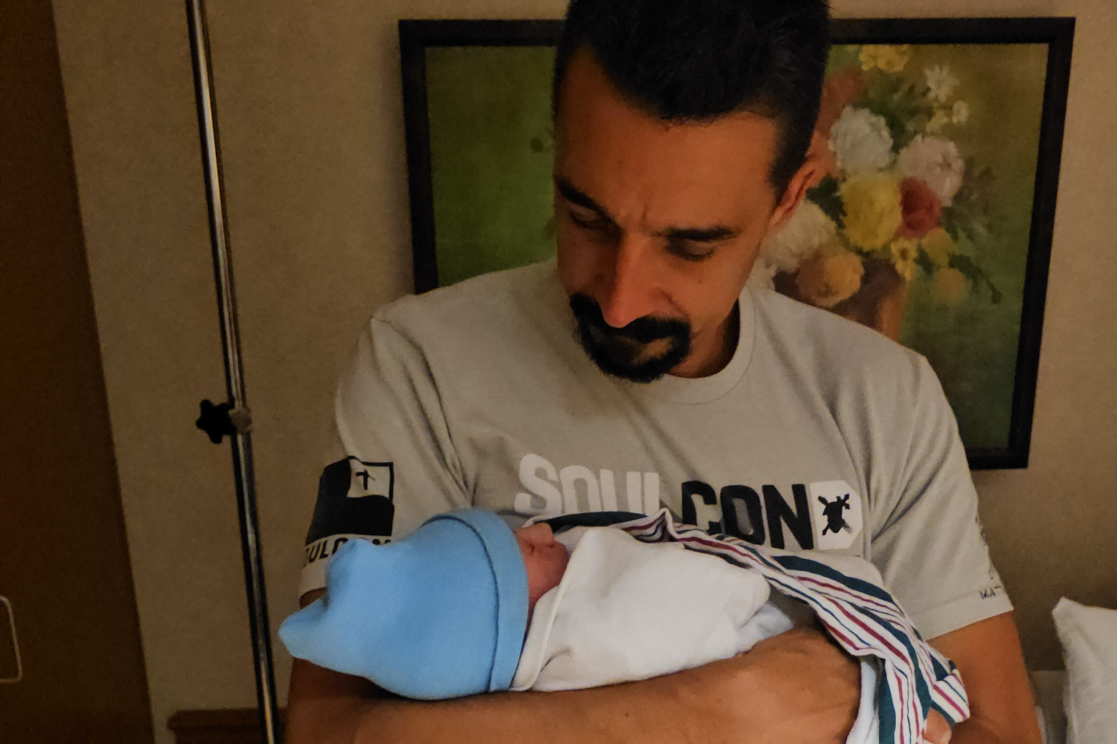 Man with short dark hair and beard cradling a newborn baby wrapped in a blue blanket
