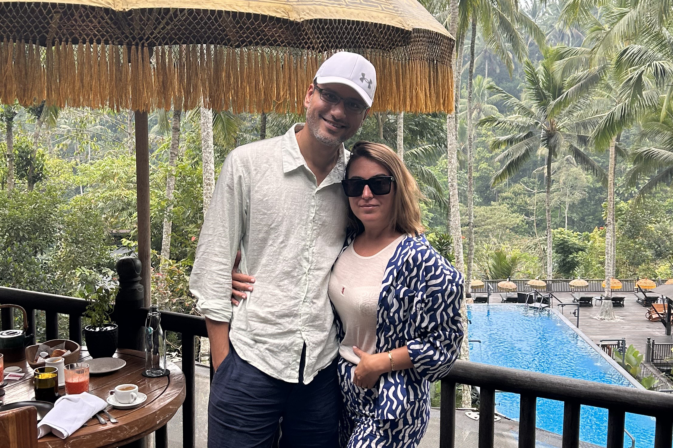 Smiling couple posing by a resort pool with palm trees in the background.