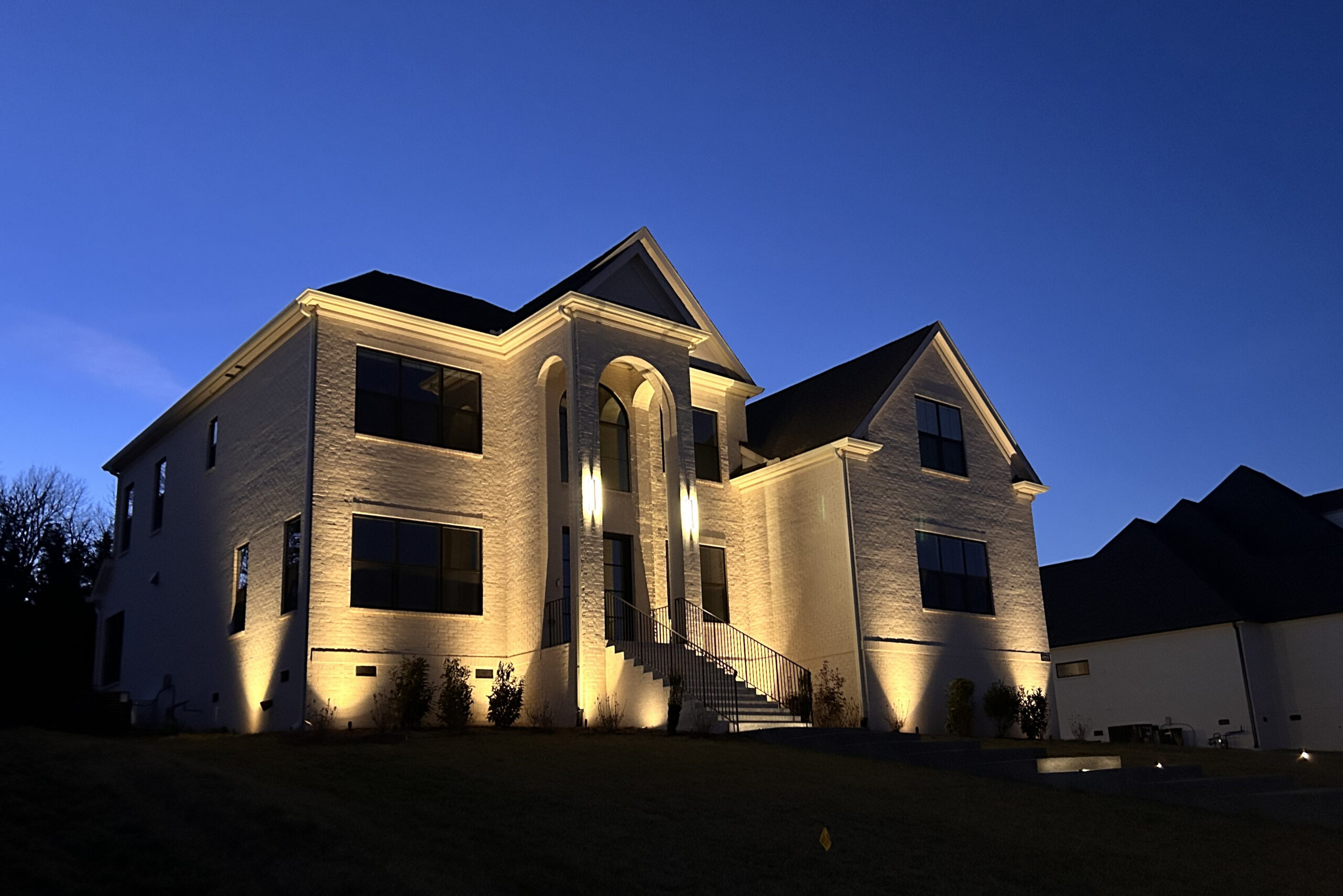 Modern brick apartment building at dusk with warmly lit entrance and stairs, blue evening sky backdrop.
