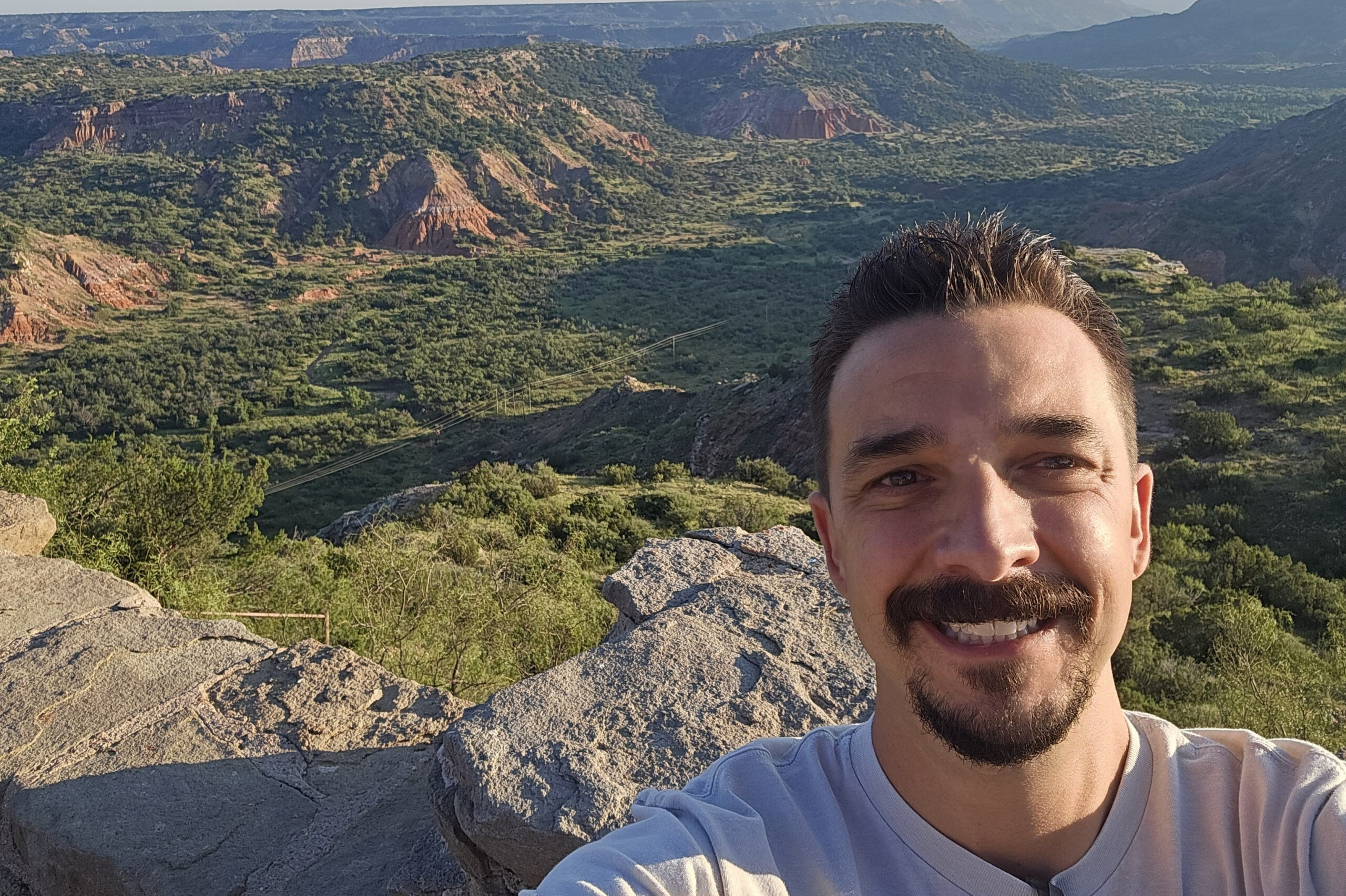 Selfie of a man with a mustache and short beard on a rocky overlook with a canyon landscape behind him.