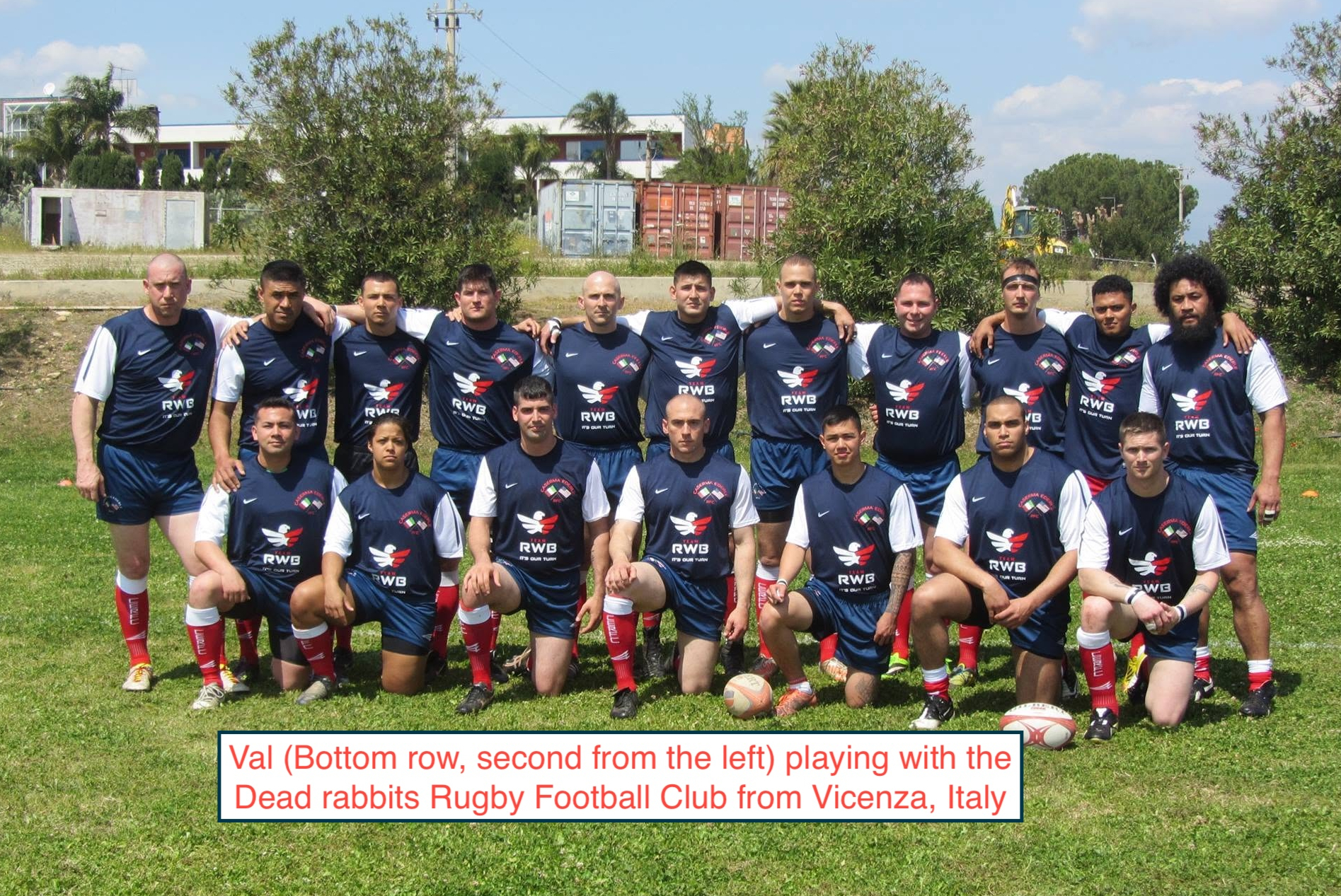 Group of rugby players in navy kits posing together on a grassy field for a team photo.