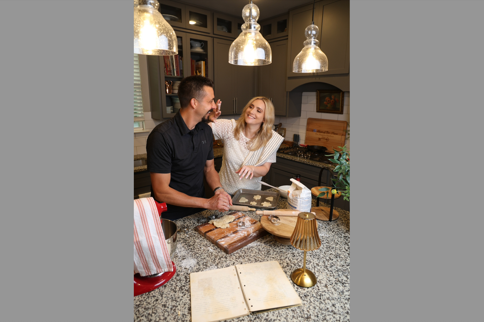 A couple laughs and bakes cookies together in a kitchen, man kneading dough while woman beams and high-fives him over the counter.