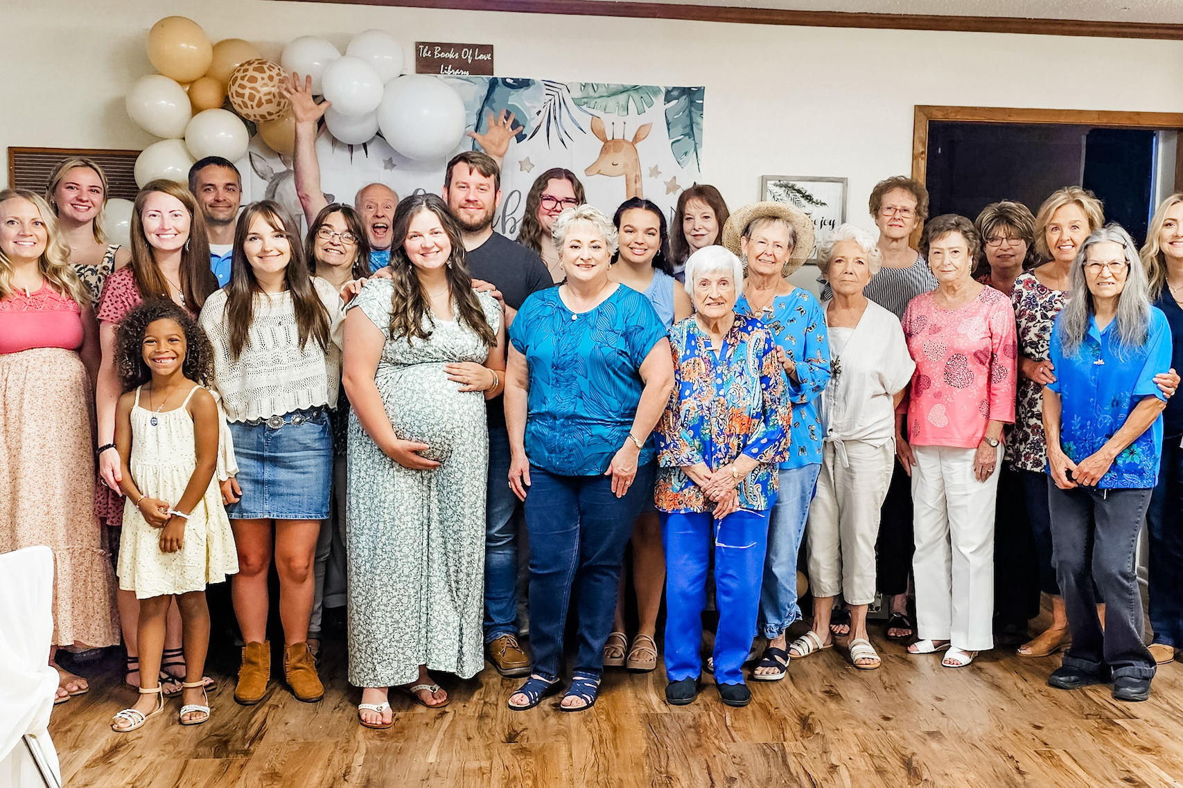 Large group portrait at a celebration with balloons and a jungle-themed backdrop behind them.