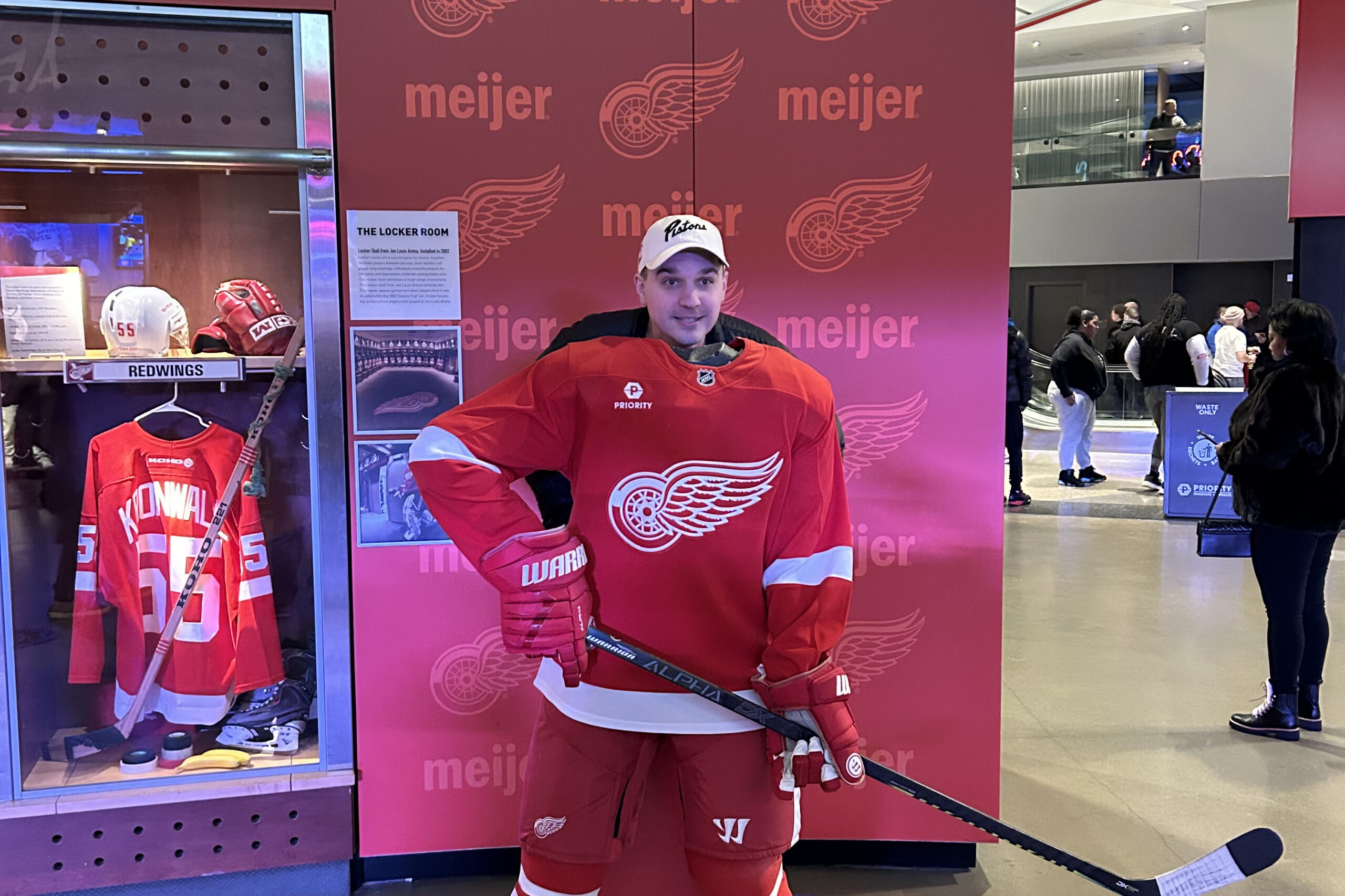 Life-sized hockey player in a red Detroit Red Wings jersey posing with a stick in front of a pink Meijer backdrop in a shopping mall display.