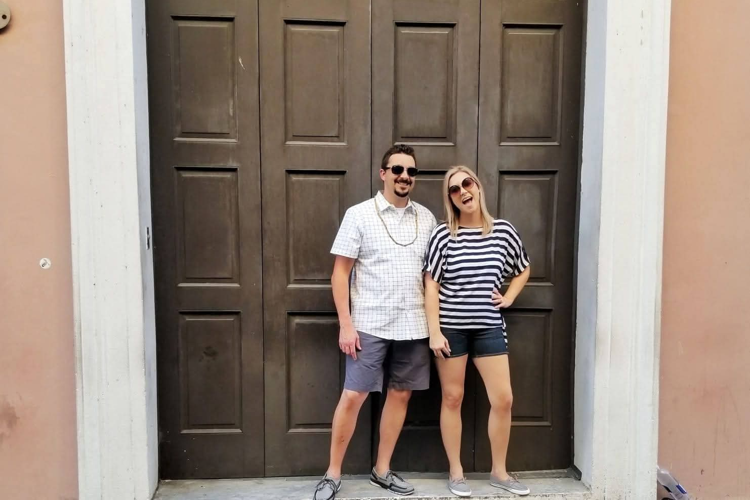 Couple posing in front of tall dark wooden doors, smiling at the camera.
