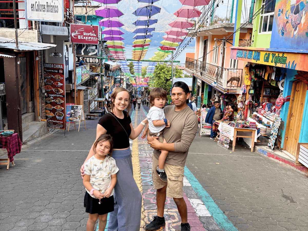 Family posing on a colorful street with umbrellas overhead and market stalls in the background.