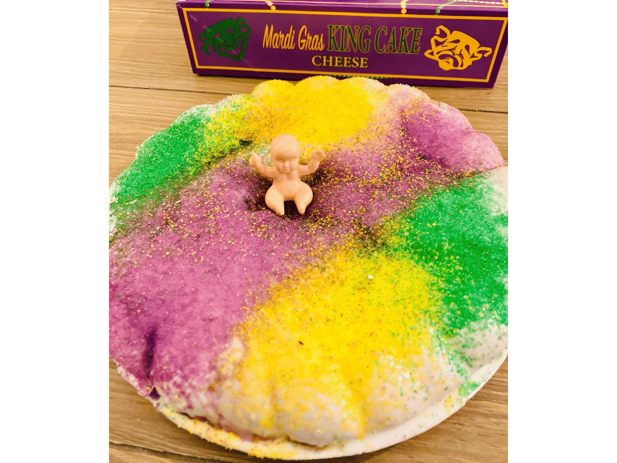 Mardi Gras king cake topped with purple, green, and yellow sugar and a small baby figurine on top