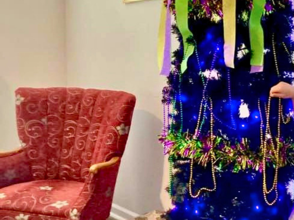 Red upholstered armchair with a patterned fabric sits beside a blue Christmas tree decorated with lights, garlands, and bead garlands in a living room.