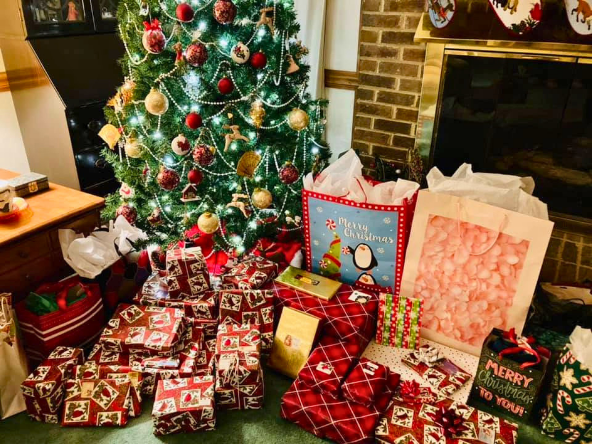 Christmas tree with lights and ornaments, surrounded by wrapped gifts and shopping bags in a cozy living room.