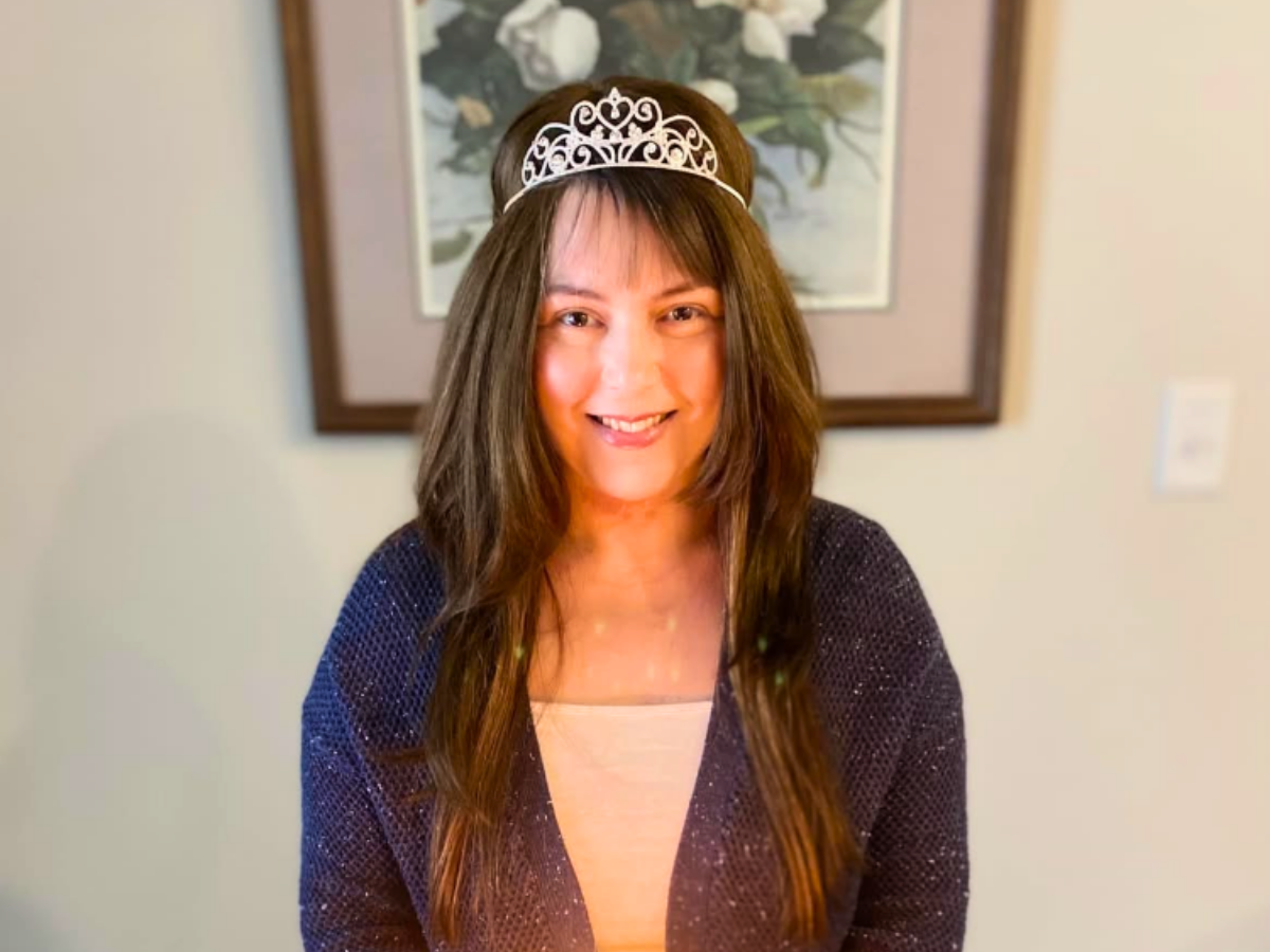 Woman with long brown hair wearing a decorative silver tiara and a dark cardigan, smiling at the camera.