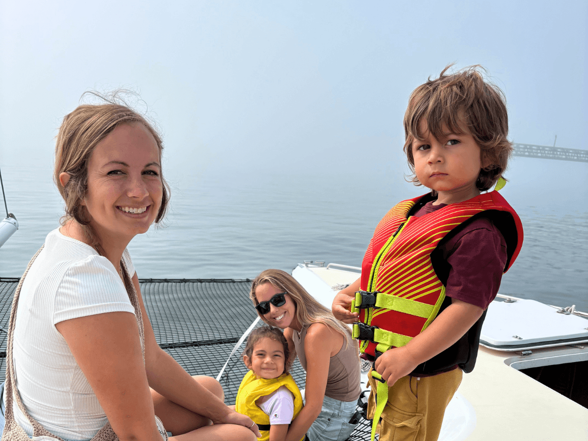 Smiling woman on a boat with two children wearing yellow life jackets; foggy lake in the background.