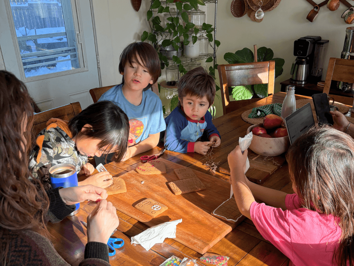 Family of children decorating gingerbread cookies at a wooden table in a cozy kitchen.
