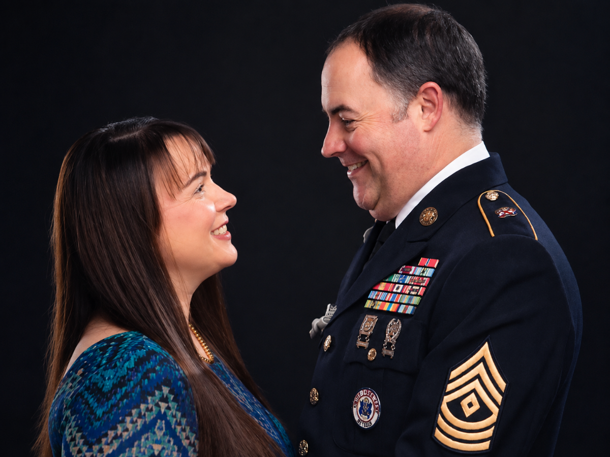 Woman and a sergeant in dress uniform smiling at each other in a studio portrait