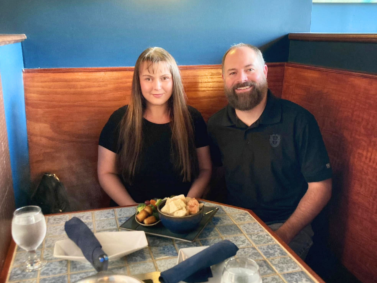 Couple dining in a blue-walled booth, smiling, with a bowl of chips and dip on the table in front of them.