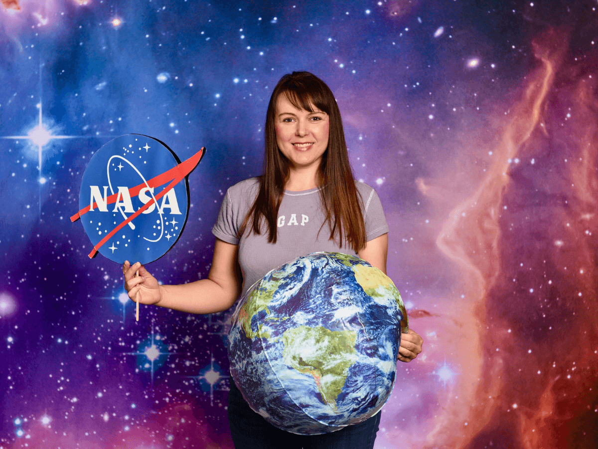 Young woman stands in a space-themed backdrop, holding a NASA sign in one hand and a large Earth globe in the other.
