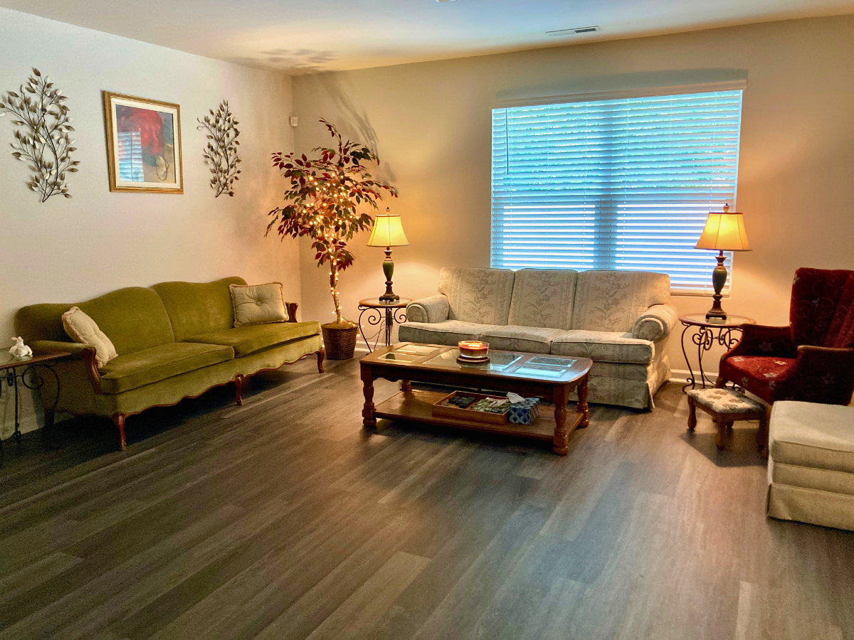 Cozy living room with a green sofa, a light floral sofa, a red armchair, two end tables with lamps, and a wooden coffee table.